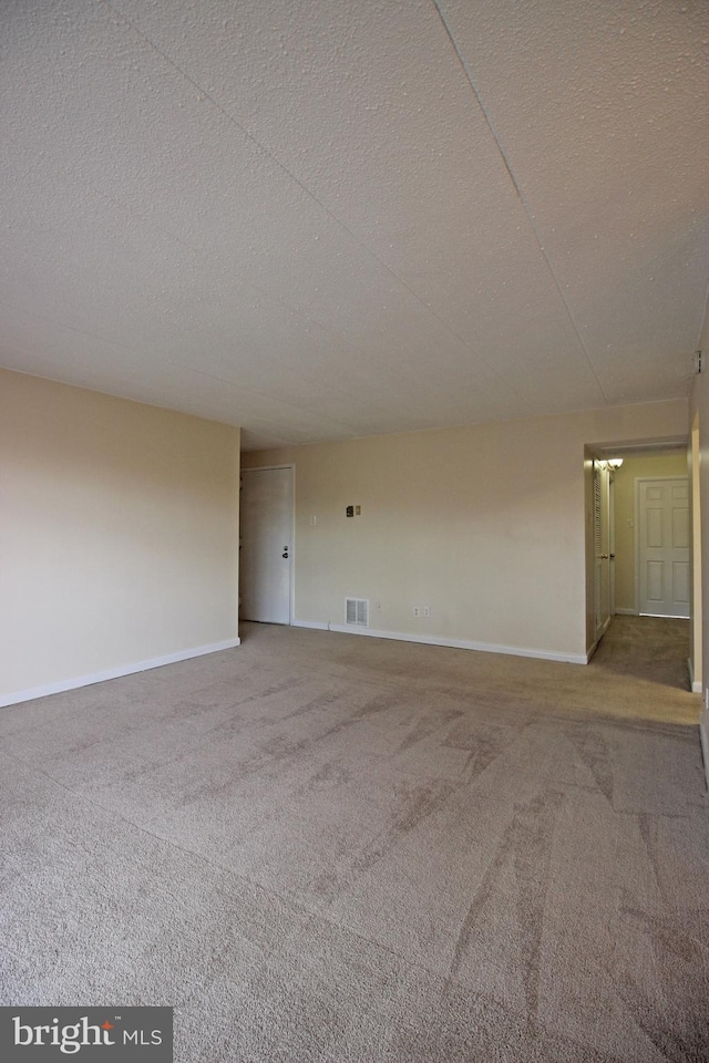 empty room featuring carpet floors, baseboards, visible vents, and a textured ceiling