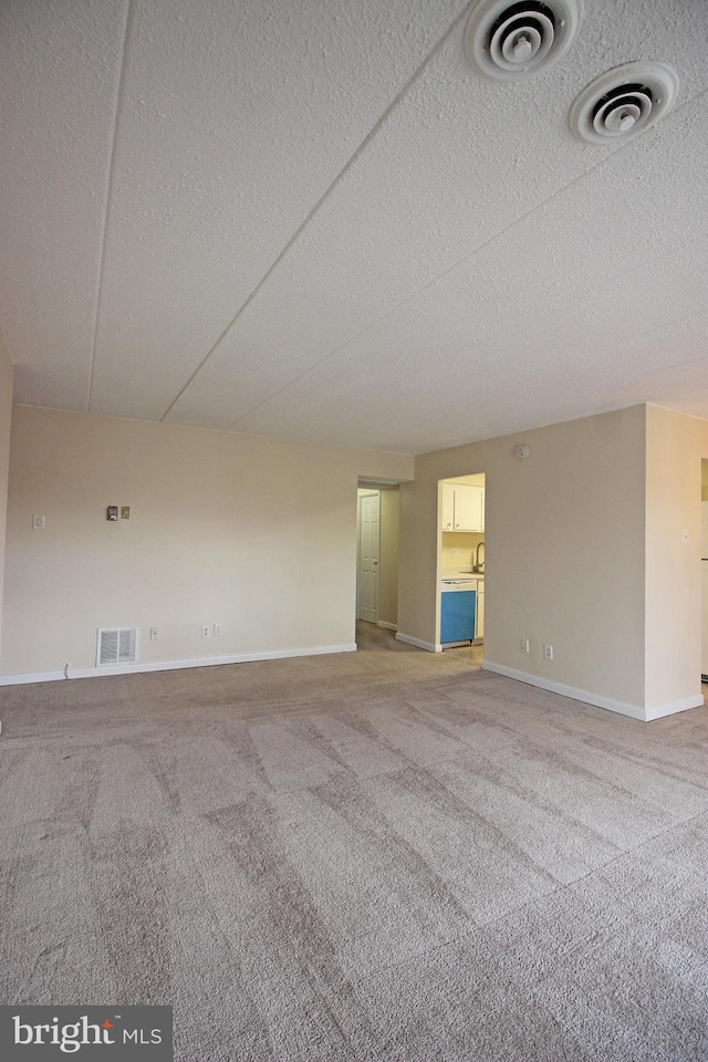 carpeted spare room featuring a textured ceiling, visible vents, and baseboards