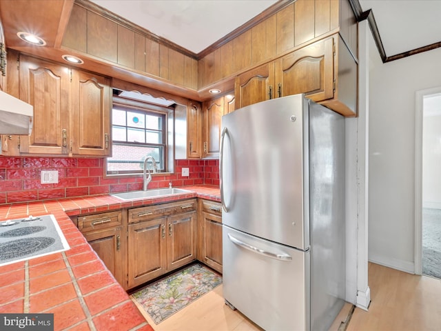 kitchen featuring crown molding, tile countertops, freestanding refrigerator, a sink, and electric stovetop