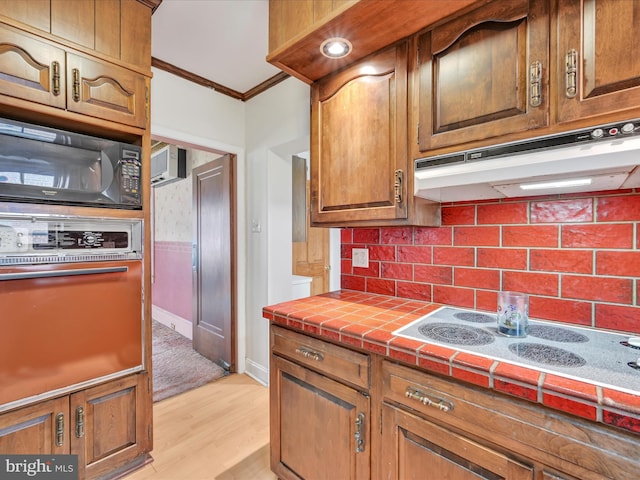 kitchen with crown molding, tile countertops, wall oven, electric stovetop, and under cabinet range hood