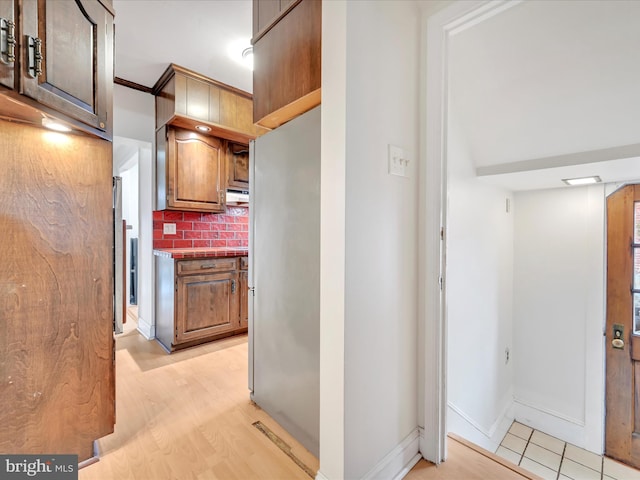 kitchen with freestanding refrigerator, backsplash, light wood-style flooring, and baseboards