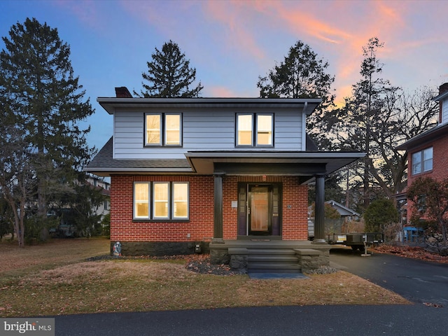 view of front of property with a chimney, aphalt driveway, a yard, a porch, and brick siding