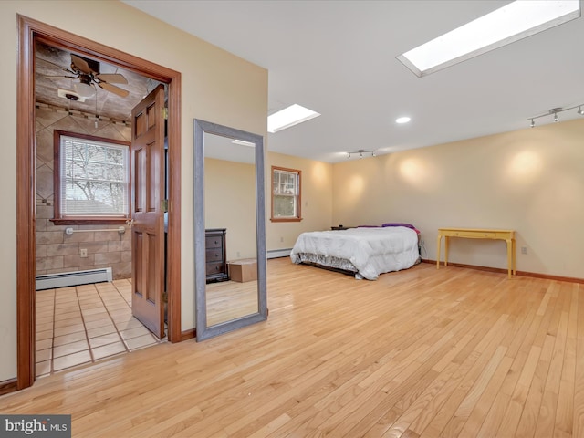 bedroom featuring light wood-style floors, baseboards, a baseboard heating unit, and track lighting