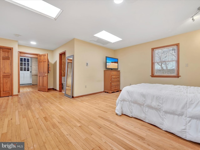 bedroom with a skylight, light wood-style flooring, and baseboards