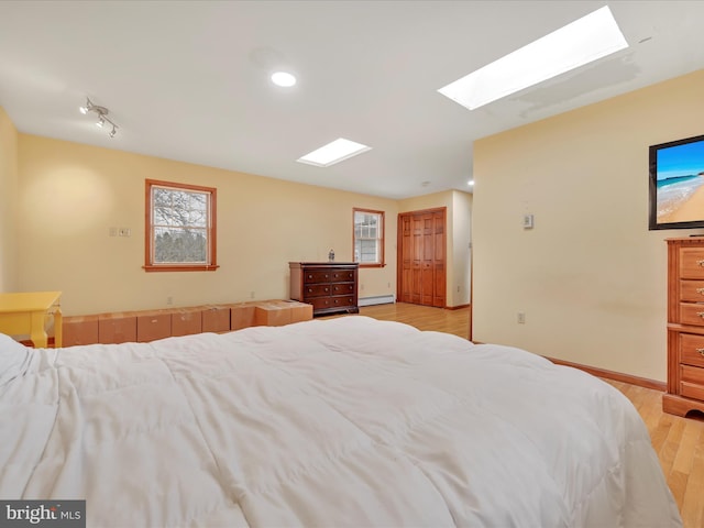 bedroom with a skylight, baseboards, light wood-style flooring, a baseboard heating unit, and recessed lighting