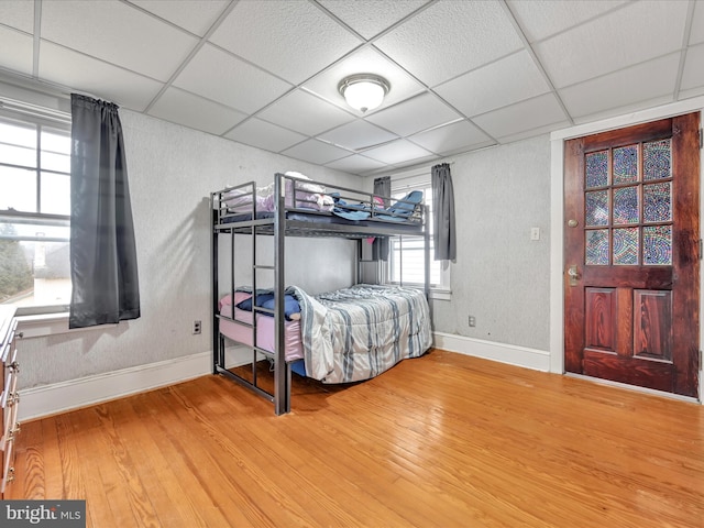 bedroom featuring a textured wall, wood finished floors, a paneled ceiling, and baseboards