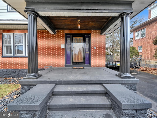 doorway to property featuring a porch and brick siding