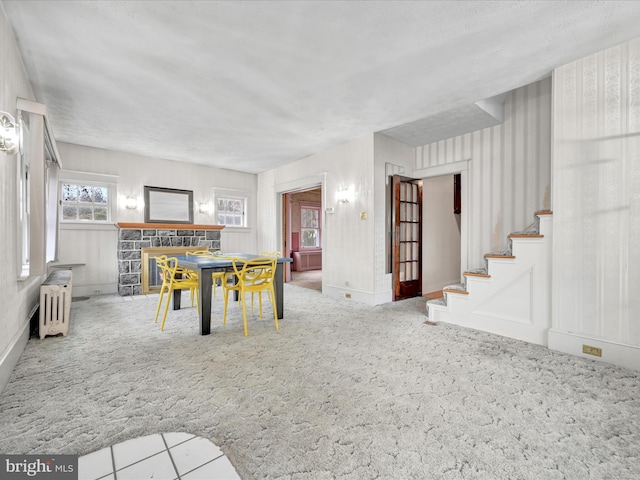 unfurnished dining area with radiator, carpet, stairway, and a stone fireplace