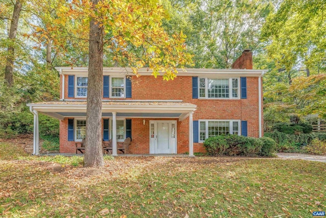 view of front of home with covered porch, a chimney, a front lawn, and brick siding