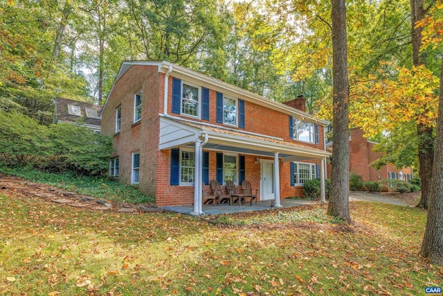 view of front of house with a porch, brick siding, a chimney, and a front lawn