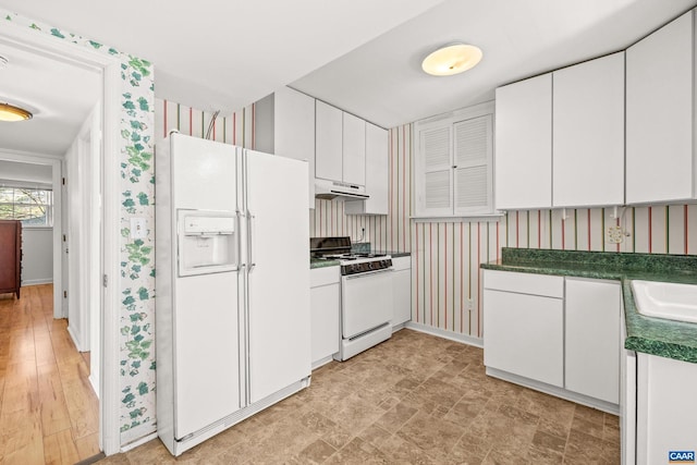 kitchen featuring white appliances, dark countertops, white cabinets, and under cabinet range hood