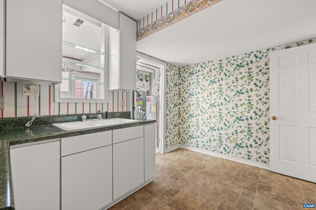 kitchen featuring white cabinetry, a sink, baseboards, and wallpapered walls