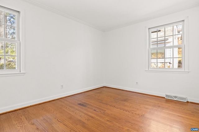 spare room featuring baseboards, light wood finished floors, visible vents, and crown molding