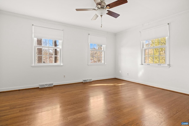 empty room featuring ornamental molding, wood finished floors, visible vents, and baseboards