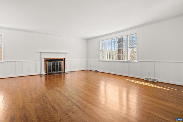 unfurnished living room with a brick fireplace, wood-type flooring, visible vents, and a wainscoted wall