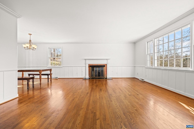 unfurnished living room with ornamental molding, wainscoting, a fireplace, and wood finished floors