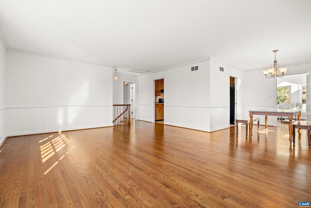 unfurnished room with an inviting chandelier, visible vents, wood finished floors, and a wainscoted wall