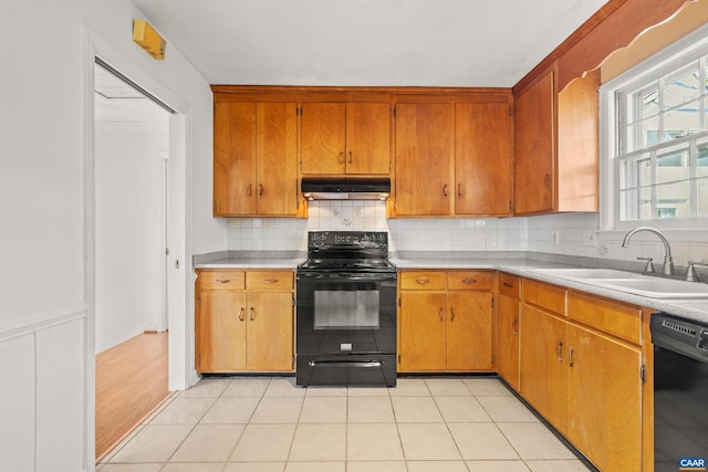 kitchen featuring tasteful backsplash, under cabinet range hood, light countertops, black appliances, and a sink