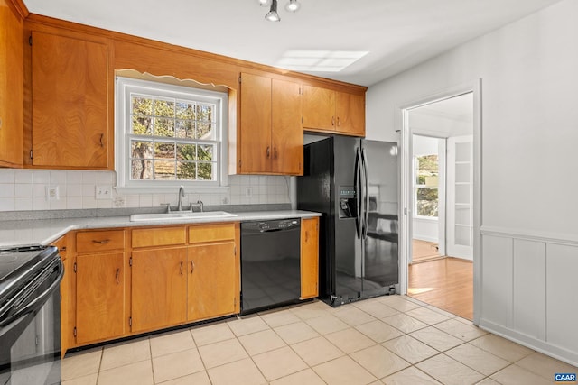 kitchen featuring a wainscoted wall, light countertops, backsplash, a sink, and black appliances