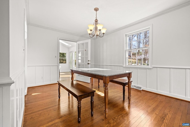 dining room with a chandelier, a wainscoted wall, ornamental molding, and hardwood / wood-style floors