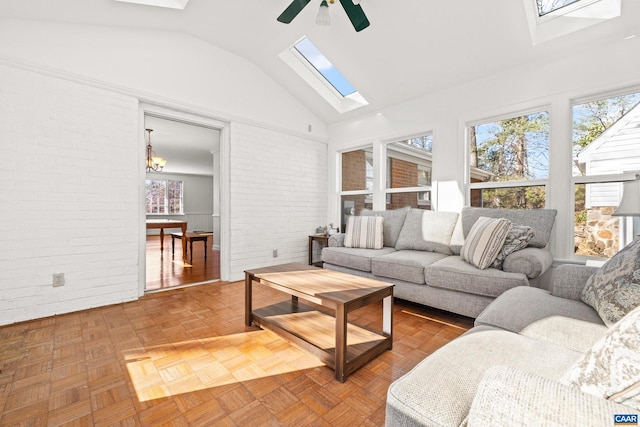 living area with ceiling fan with notable chandelier, brick wall, a skylight, and high vaulted ceiling