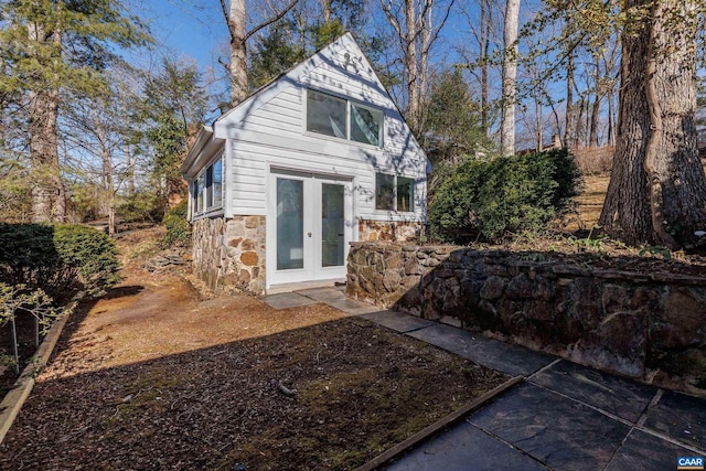 back of property with stone siding, french doors, and an outdoor structure