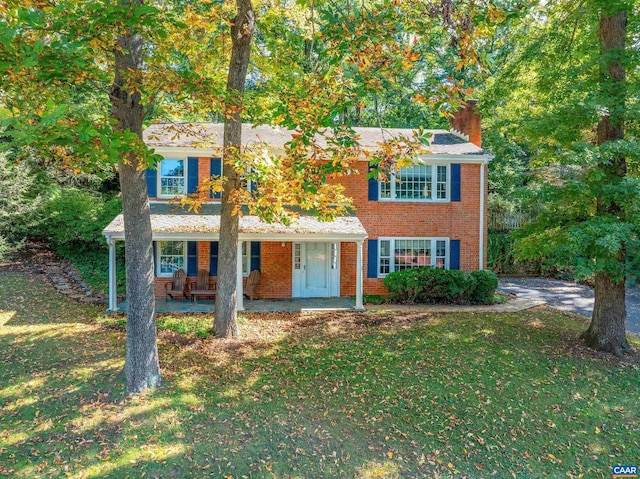 view of front of home with covered porch, a front lawn, a chimney, and brick siding