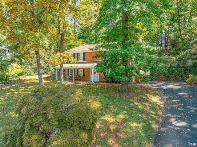 view of front of property featuring driveway, covered porch, brick siding, and a front yard