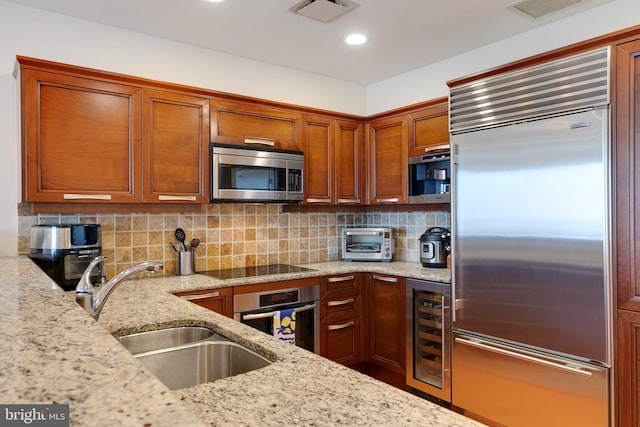 kitchen with light stone counters, wine cooler, stainless steel appliances, a sink, and visible vents