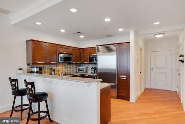 kitchen with light stone counters, a breakfast bar area, stainless steel appliances, a peninsula, and light wood-style floors