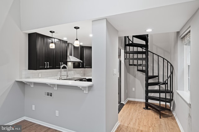 922 Clinton St, Philadelphia, PA 19107 - kitchen featuring wall chimney range hood, dark cabinets, tasteful backsplash, a breakfast bar, and light wood-style flooring