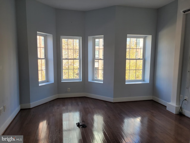 empty room featuring dark wood-style floors, a wall mounted air conditioner, and baseboards