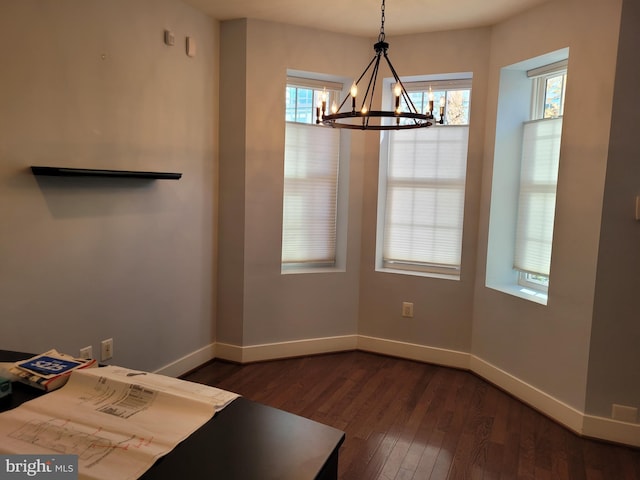 unfurnished dining area featuring dark wood-type flooring, an inviting chandelier, and baseboards