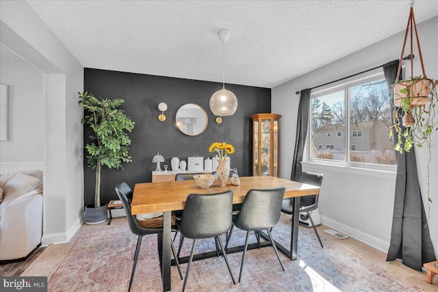 dining room featuring an accent wall, visible vents, a textured ceiling, and baseboards