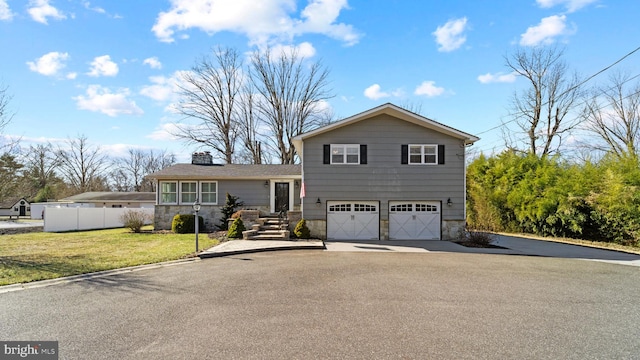 tri-level home with driveway, a garage, stone siding, fence, and a front lawn