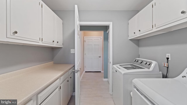 clothes washing area featuring light wood-style floors, baseboards, cabinet space, and washing machine and clothes dryer