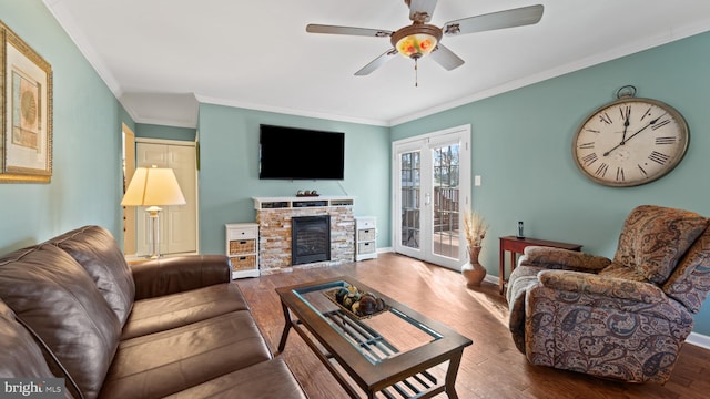 living room featuring a ceiling fan, crown molding, baseboards, and wood finished floors