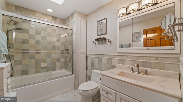 bathroom with toilet, bath / shower combo with glass door, vanity, tile walls, and wainscoting