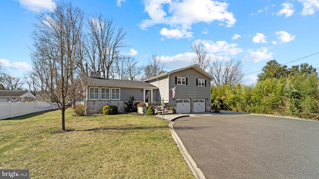 split level home with a garage, a chimney, aphalt driveway, fence, and a front lawn