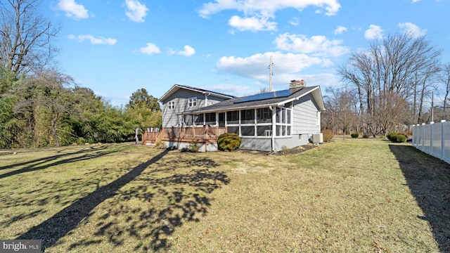 exterior space with central AC unit, a sunroom, a lawn, roof mounted solar panels, and a chimney