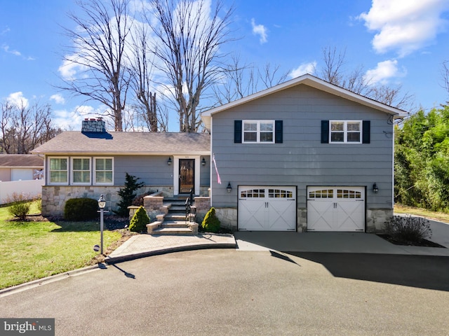 tri-level home featuring driveway, a garage, stone siding, a chimney, and a front yard