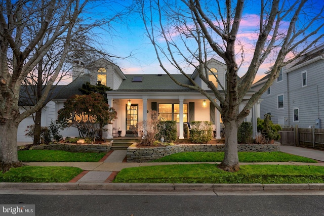 view of front of house featuring roof with shingles, stucco siding, a porch, a lawn, and fence