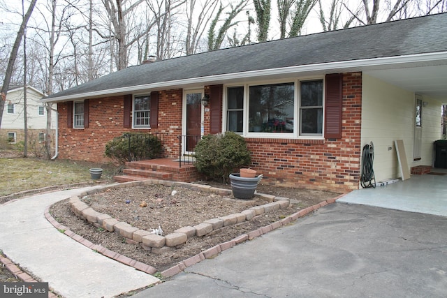 ranch-style home featuring an attached carport, brick siding, driveway, and roof with shingles