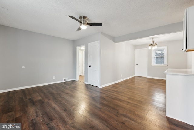 unfurnished living room with visible vents, a textured ceiling, baseboards, and dark wood-type flooring