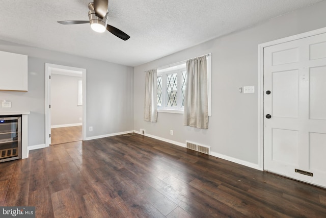 unfurnished living room featuring baseboards, visible vents, dark wood-style floors, wine cooler, and a textured ceiling