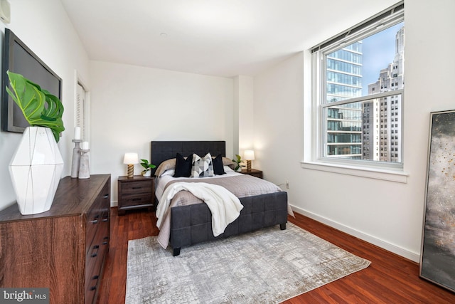 bedroom with dark wood-style floors, a view of city, and baseboards