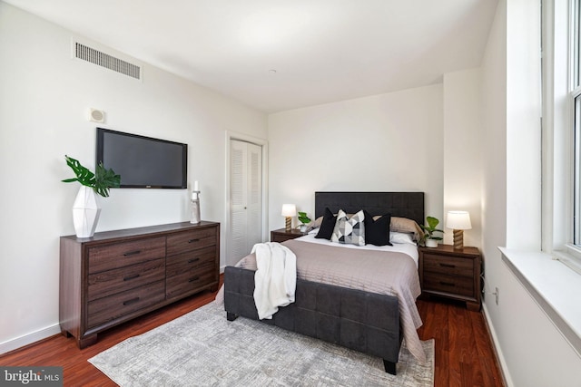 bedroom with dark wood-style flooring, a closet, visible vents, and baseboards