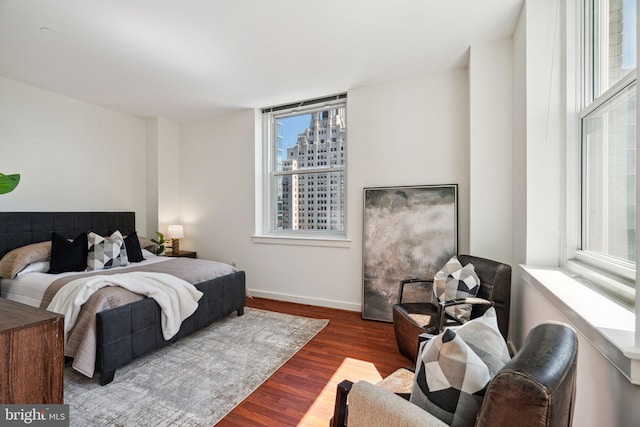 bedroom with a view of city, multiple windows, wood finished floors, and baseboards