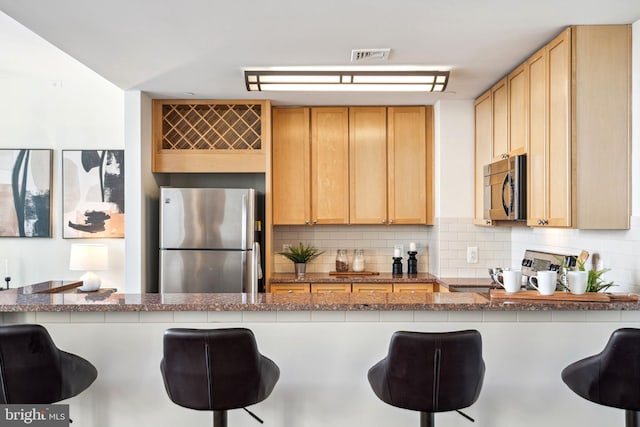 kitchen with light stone counters, stainless steel appliances, backsplash, and a kitchen breakfast bar