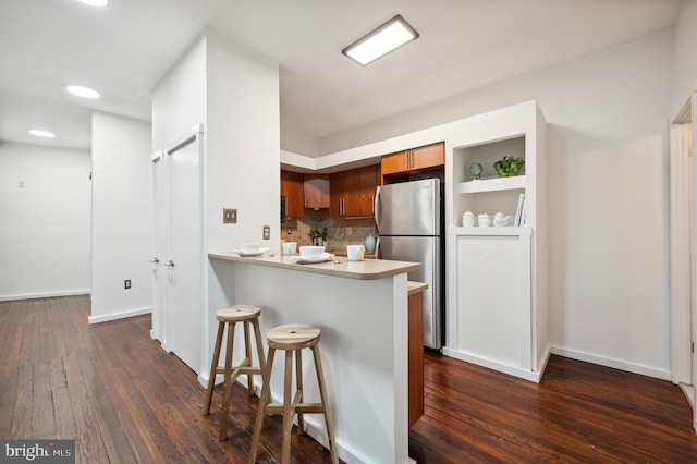 kitchen with a breakfast bar area, brown cabinets, dark wood-type flooring, freestanding refrigerator, and light countertops